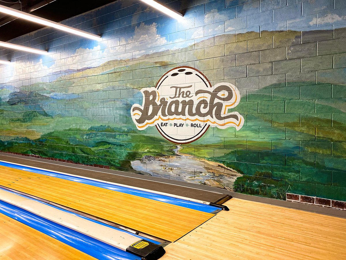 The Branch | A local bowling alley transforms into a Restaurant Bar Arcade with Lanes | Aird Designs uses Graphics, Illustrations and a large "Long Way" Mural of the Blue Ridge Mountains through a breakaway brick way to transform the space and promote community.